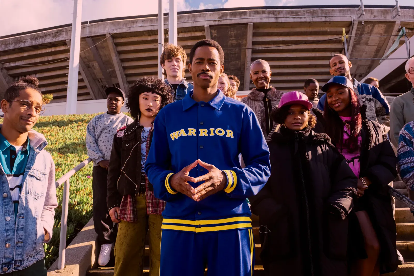 A publicity still from "Freaky Tales," with Jay Ellis and other actors standing in front of the Oakland Coliseum. Ellis is wearing 1980s-style Golden State warmups, which look cool as shit.